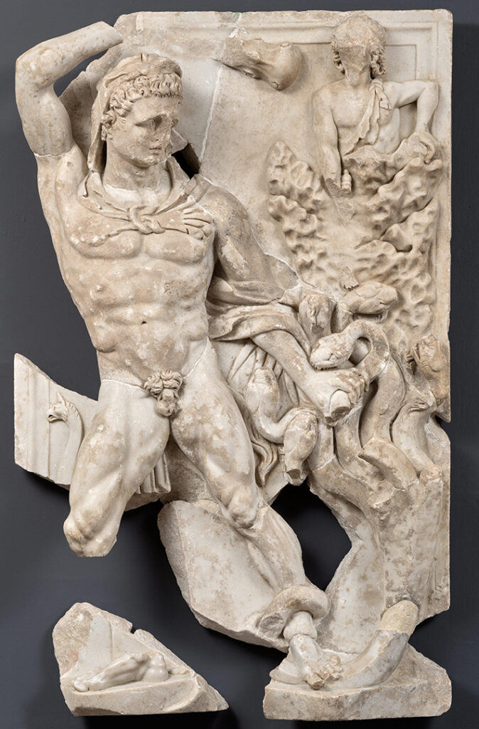 Relief représentant Hercule et l’hydre de Lerne. Le relief est en marbre blanc. Il est en forme de rectangle, à la verticale, et la bordure est sculptée comme un cadre. Plusieurs parties du relief ont été cassées et sont manquantes. Occupant la partie gauche de sculpture, Hercule lève le bras droit. Il est nu, à l’exception d’une peau de lion qui lui couvre la tête et dont les pattes sont nouées sur sa poitrine. Dans sa main droite, il tient une massue. Son autre main est baissée, et tient un monstre. Il s’agit d’un serpent à plusieurs têtes, l’hydre de Lerne. Au-dessus de l’hydre se trouve un personnage dont la taille est réduite par rapport à celle d’Hercule. La scène est lacunaire, mais il était en train de brûler les têtes de serpents.