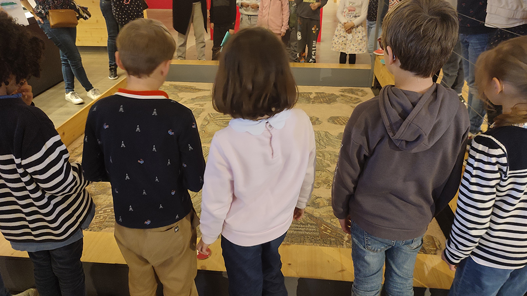 Un groupe d'enfants est rassemblé autour de la mosaïque découverte à Saint-Rustice