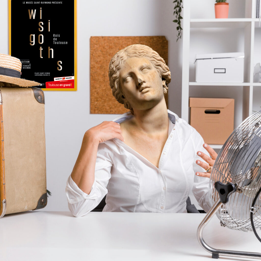 Une femme, dont la tête a été remplacée par une tête sculptée, prend le frais devant un ventilateur.