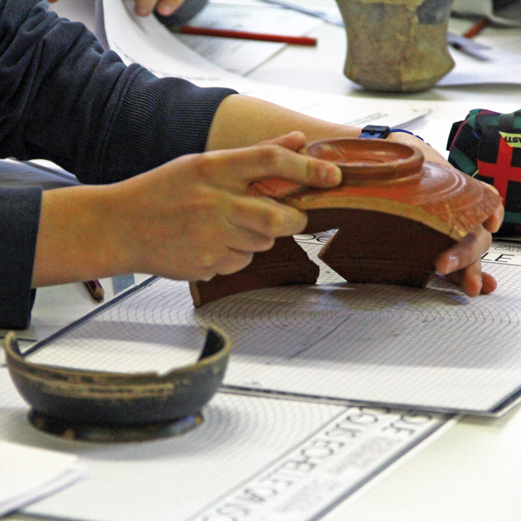 Un élève essaye de déterminer le diamètre d'une céramique romaine qu'il tient dans ses mains.
