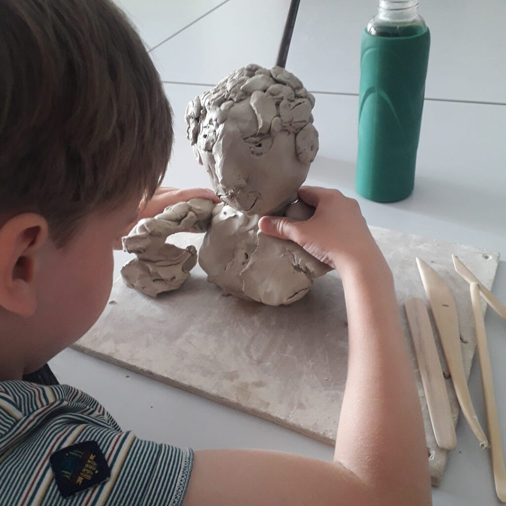 Un jeune garçon modèle un buste humain avec de l'argile.