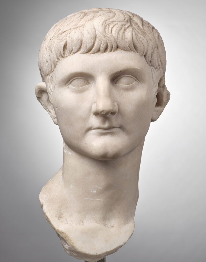 Portrait sculpté de Germanicus vu de face. Le portrait en marbre blanc représente un homme jeune. La base de son long cou est arrondie pour être encastrée dans un support. Il est bien conservé, seule la pointe de son oreille gauche manque. Son menton est marqué au centre par une fossette. Il ne porte pas de barbe. Sa bouche est fine, et les commissures de ses lèvres sont bien marquées. Son expression est neutre. Le nez est presque aussi large que la bouche ; il est plutôt volumineux et comporte une légère bosse. Les pupilles ne sont pas représentées : il a les yeux lisses. Des mèches légèrement ondulées mais plates retombent sur son front. Son oreille droite est légèrement décollée.