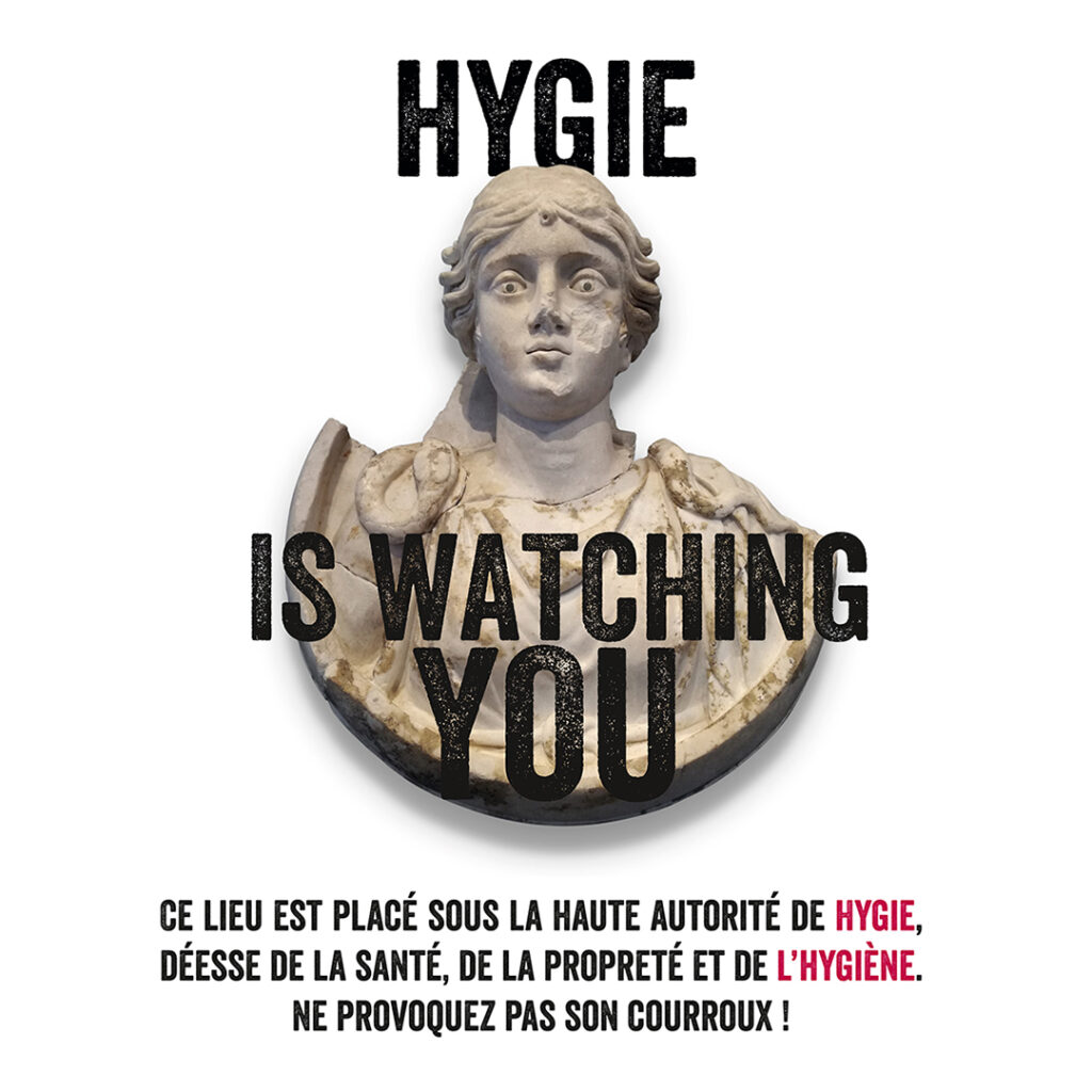 Médaillon sculpté en marbre représentant la déesse romaine Hygie. Texte : Hygie is watching you. Ce lieu est placé sous la haute autorité de Hygie, déesse de la santé, de la propreté et de l'hygiène. Ne provoquez pas son courroux !
