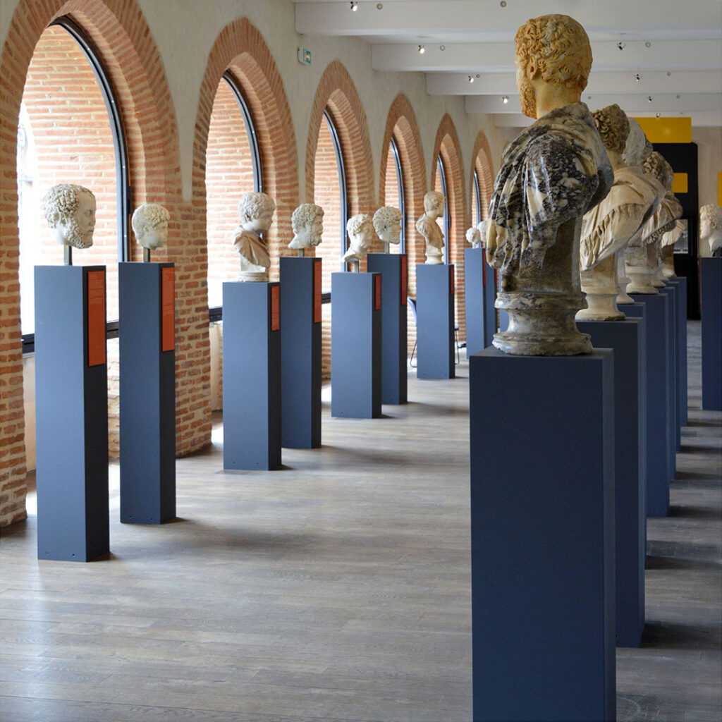Vue de la galerie des portraits du musée : on y voit des bustes romains en marbre placés sur des socles hauts.