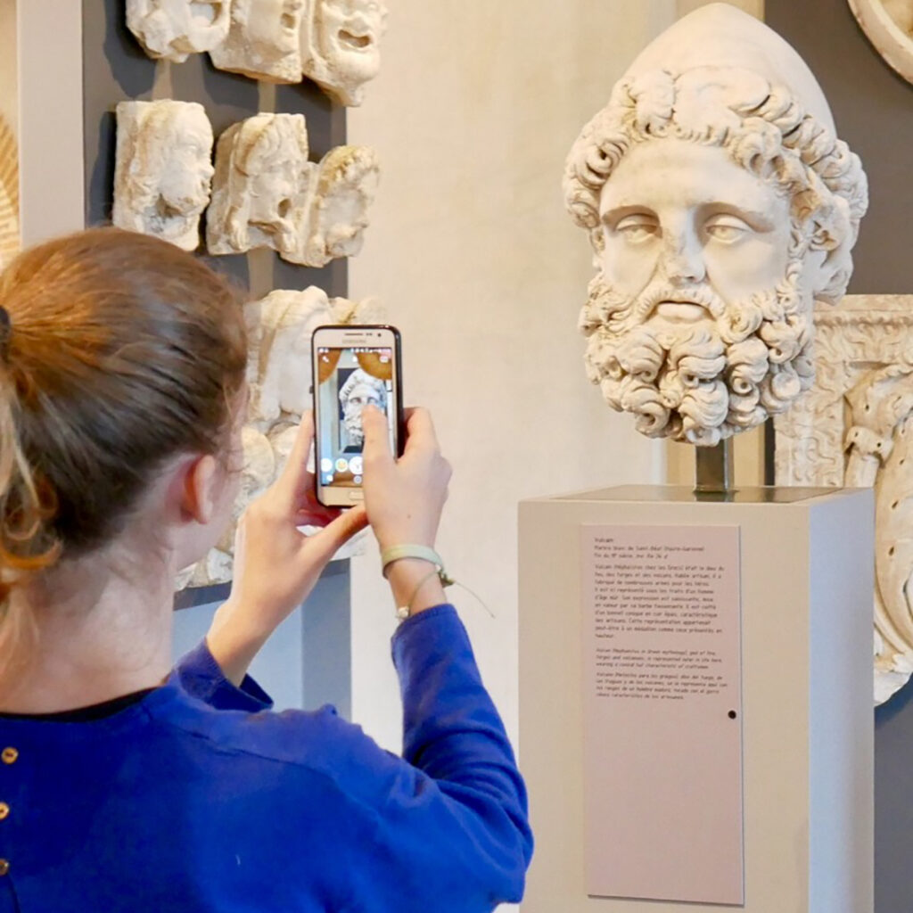 Une jeune femme prend en photo avec son smarphone une tête sculptée en marbre.
