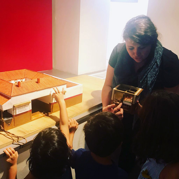 Une médiatrice montre à des enfants des éléments d'une maquette de maison romaine.
