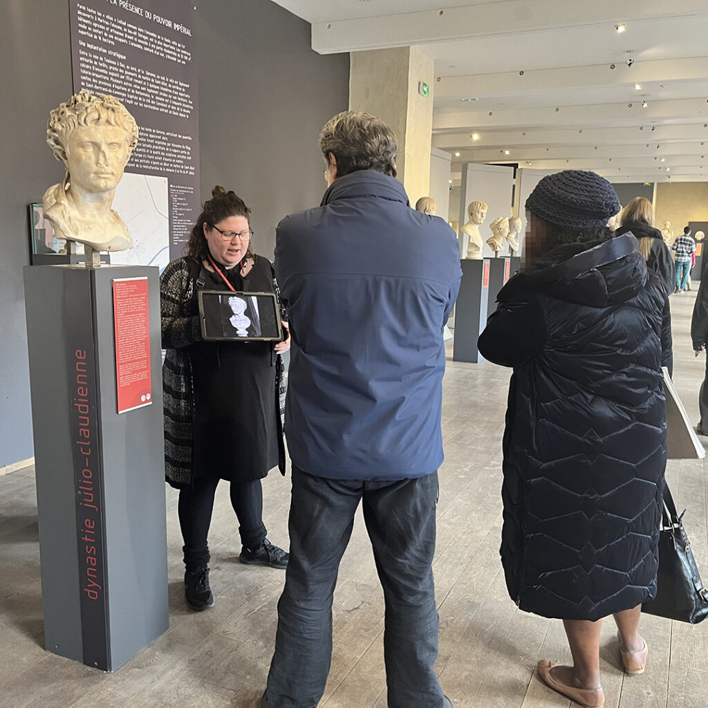 Deux personnes, de dos, assiste à la visite "Secrets de conservation" au cours de laquelle est abordée le cas d'un buste en marbre représentant l'empereur Auguste.