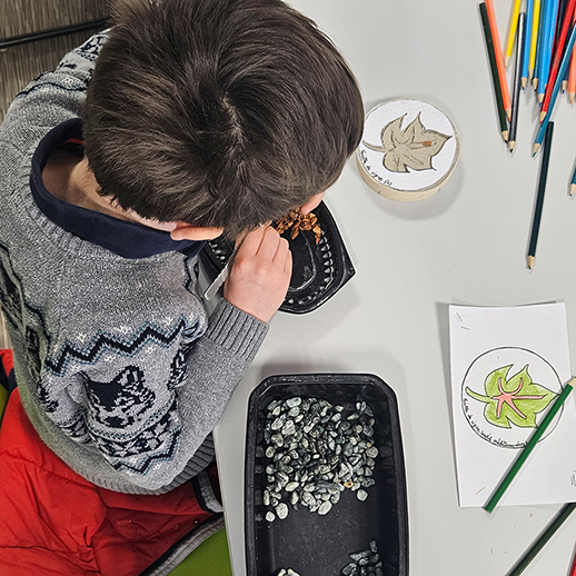 Un enfant réalise une mosaïque en forme de feuille à l'aide de petits galets.